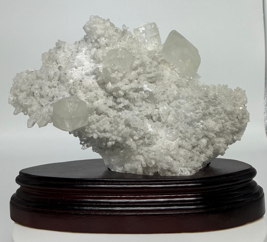 Calcite and Quartz crystal cluster on a wooden stand against a white background