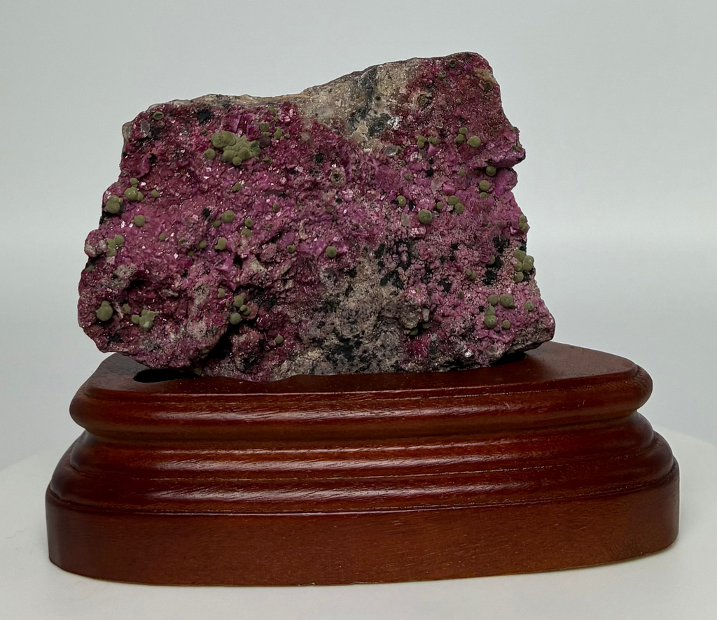 Purple mineral specimen on a wooden stand against a white background
