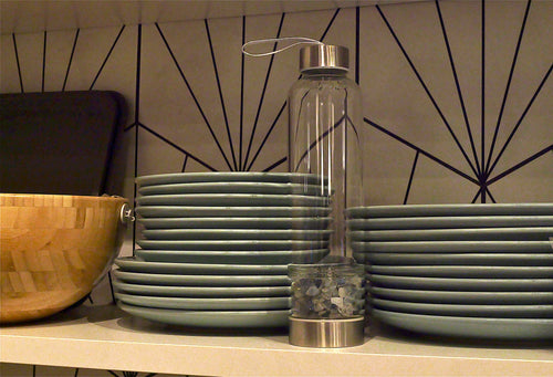 Stacks of green plates with a clear bottle on a shelf against a geometric wall pattern.